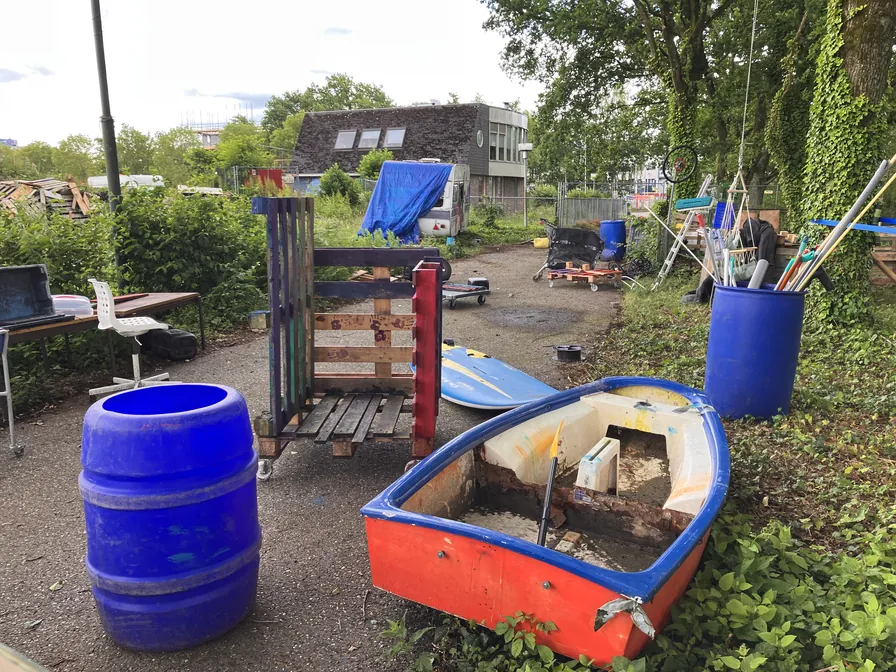 Een blauw vat, houten pallets, een omgebouwde boot en gereedschap in de openlucht bij de Avonturenspeeltuin