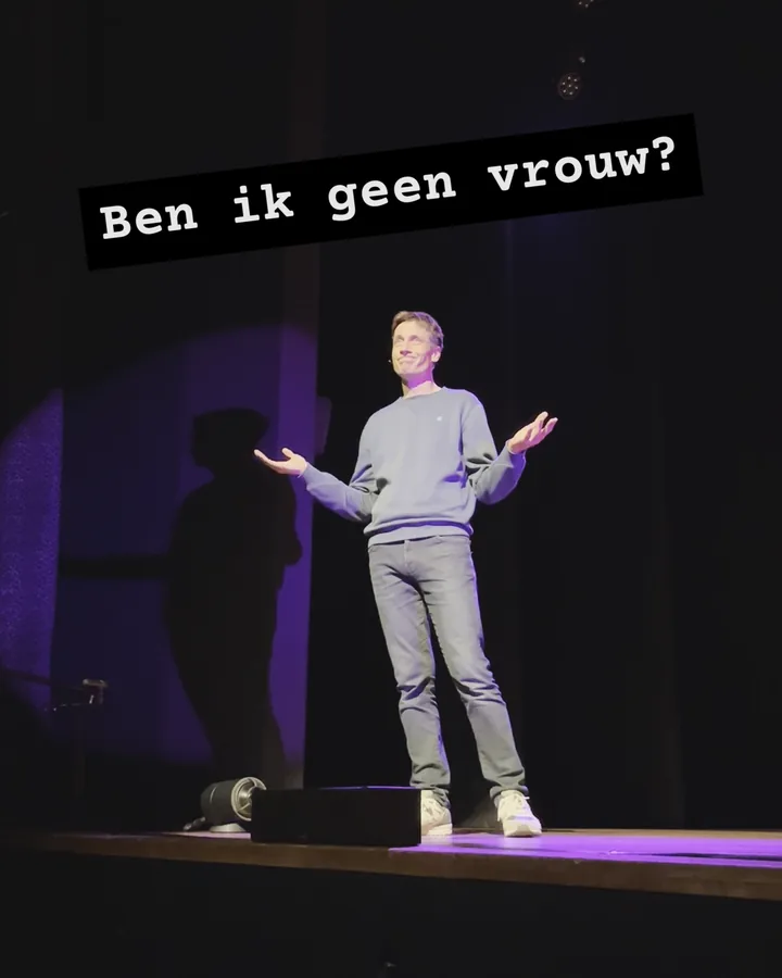 Floris Huetink op een paars verlicht podium, schouders opgehaald en handen open, met daarboven de titel ‘Ben ik geen vrouw?’